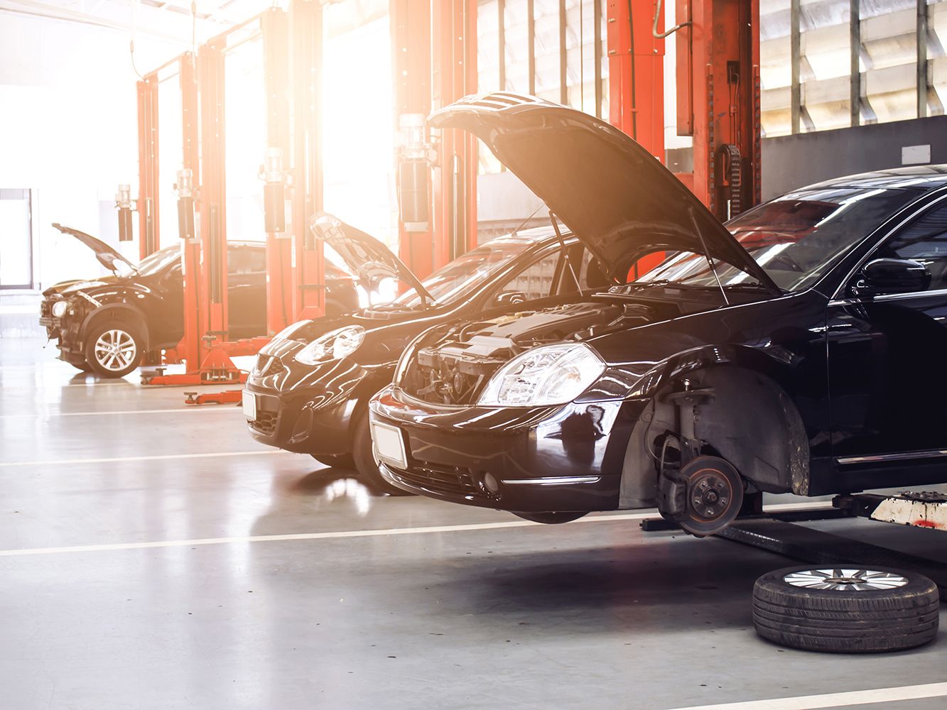 Innenansicht einer Kfz-Werkstatt | Drei schwarze Autos mit geöffneten Motorhauben auf Hebebühnen.